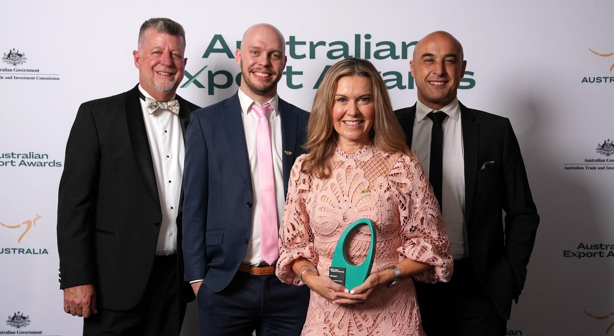 Four MyVenue Team Members are pictured smiling in front of the 2023 Australian Export Awards Banner. One team member is carrying a trophy.