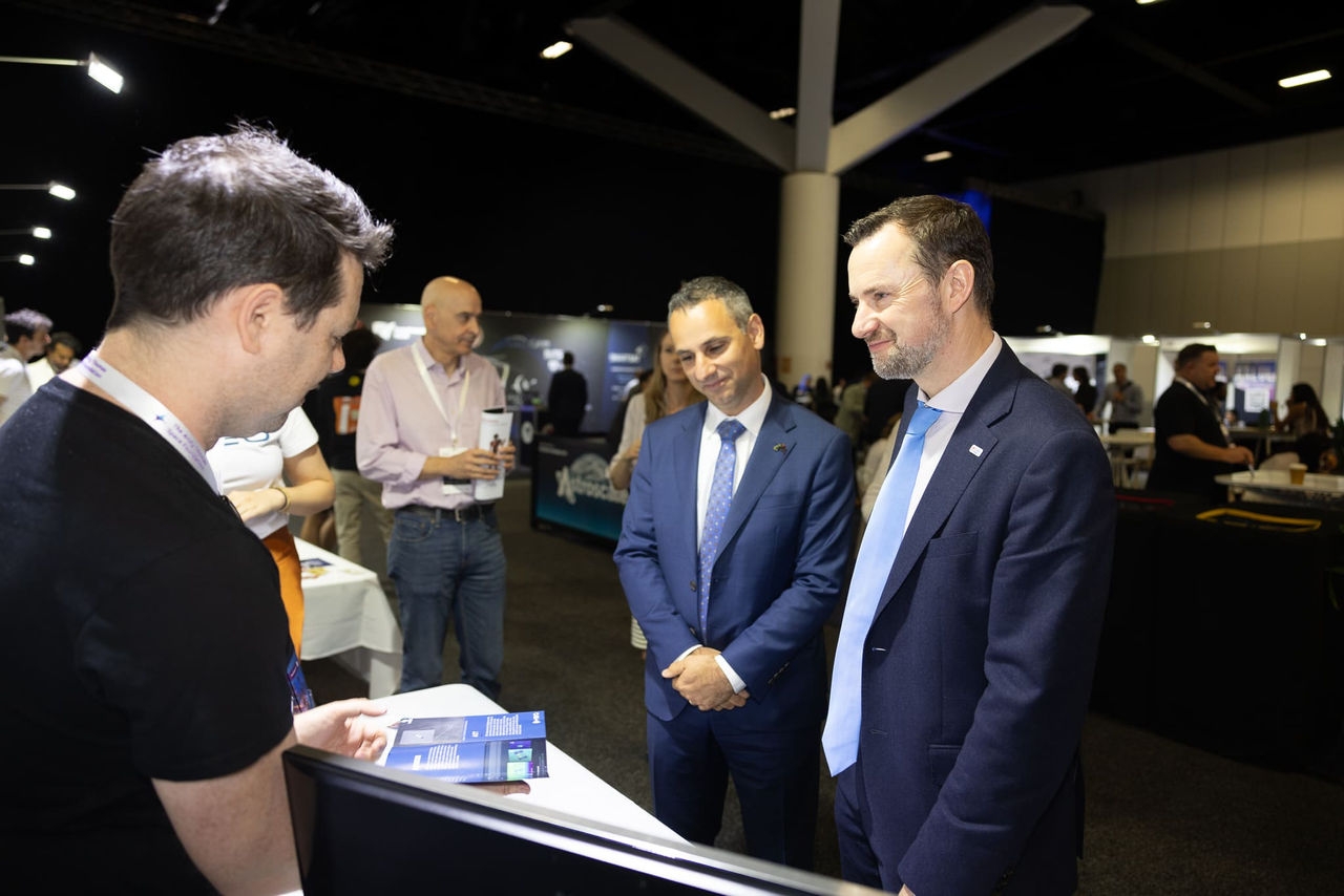 Two men in suits speaking with a third man in a black T-shirt. 