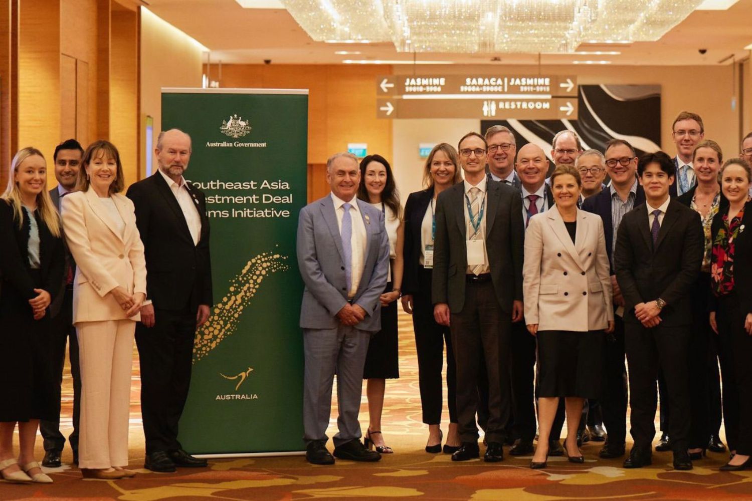 A delegation of men and women in business attire stand next to a banner for a group photo.