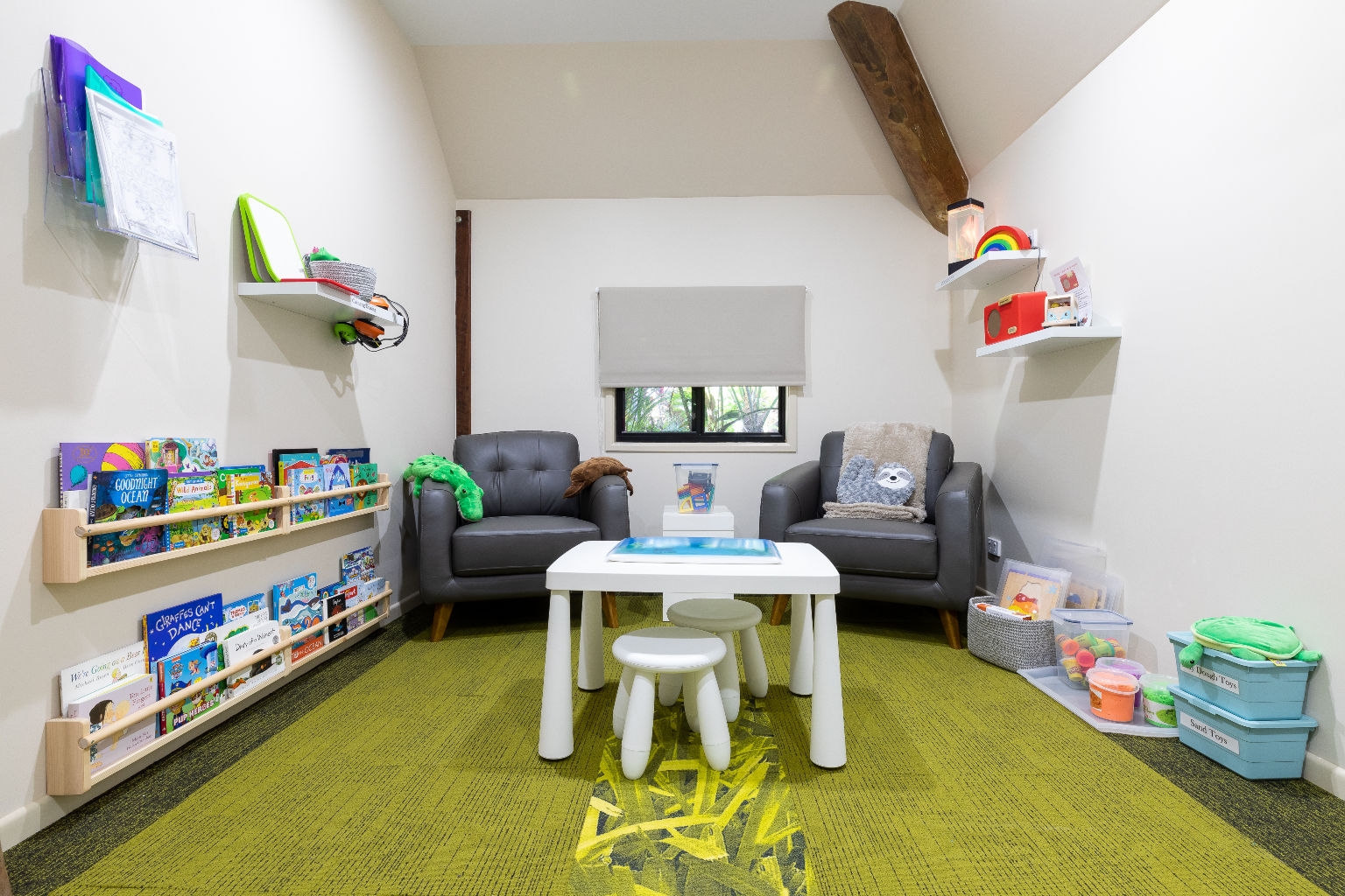 A room with two armchairs, a kid-sized table and two chairs, and shelves of books on the left.