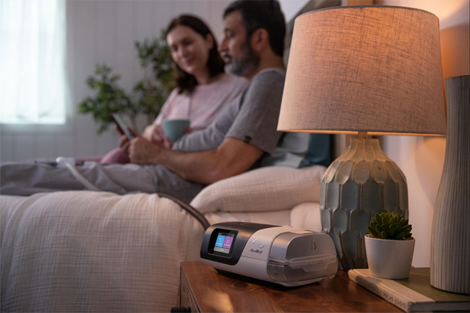 Couple sitting on bed with a Resmed device on the bedside table