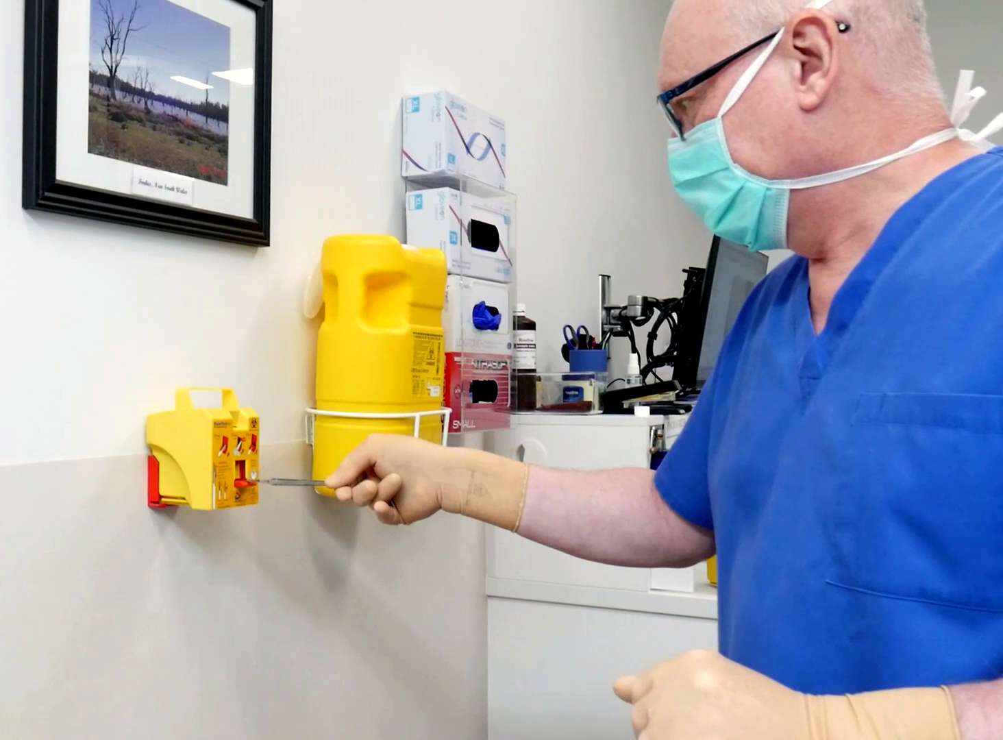 A man in scrubs and a surgical mask removing a scalpel blade using Qlicksmart's scalpel blade remover device.