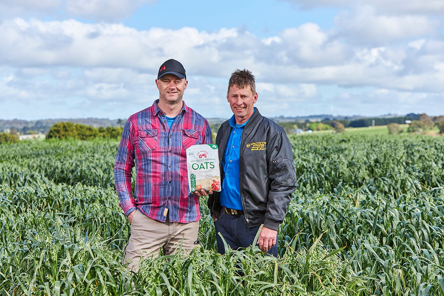 Kane and Mike Nagorka of Waltanna Farms standing in an oat crop field, holding up a packet of oats