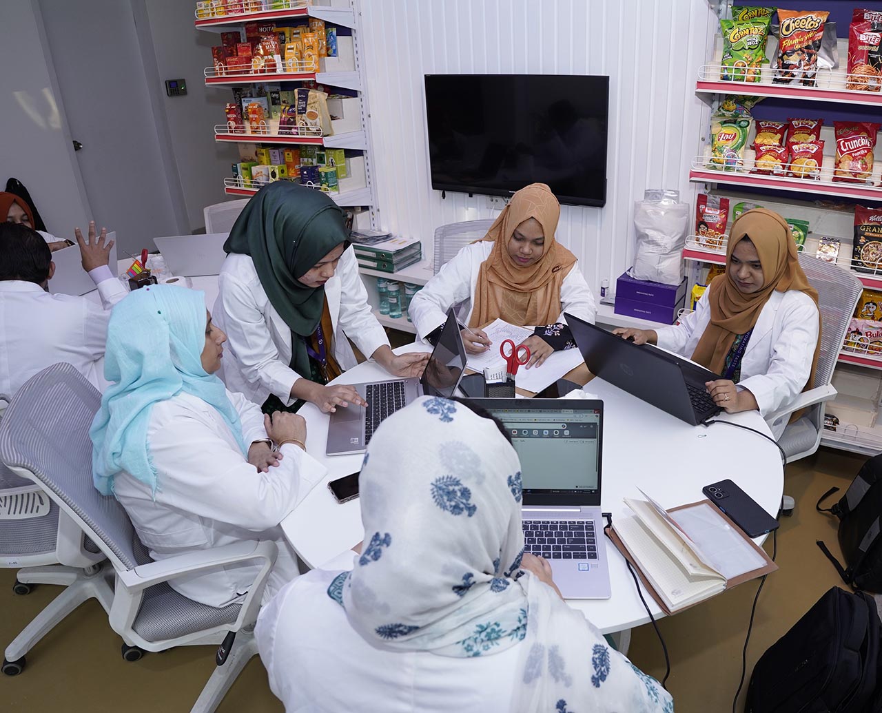 5 women sitting around a round table working on laptops