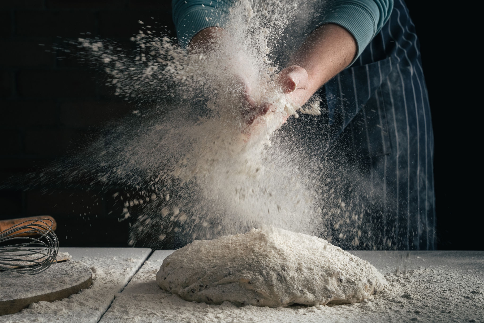 Pre-baked sourdough on a bench, with flour bursting from a baker's hands.