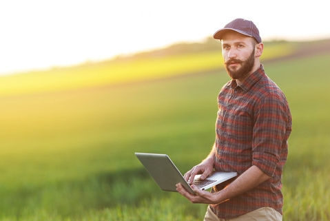 Unrecognizable young farmer using laptop on field. Panoramic view of farmer standing in field.